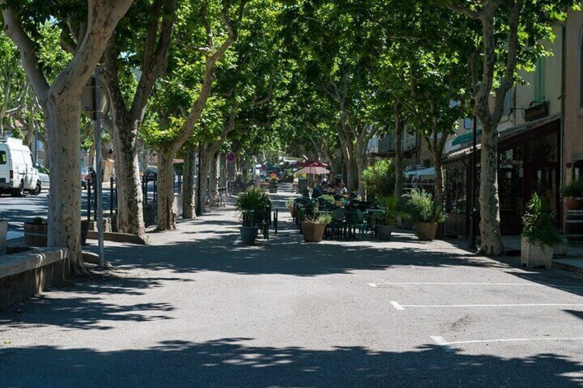 A tree-lined street with outdoor seating, parked cars, and buildings. 2