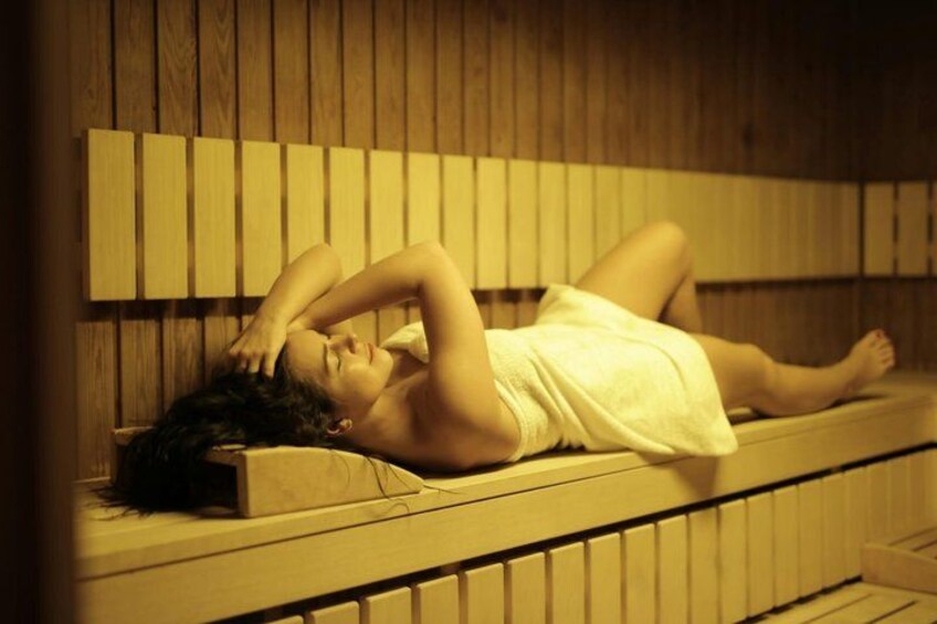 Eine Person liegt auf einer Holzbank in einer Sauna. 5