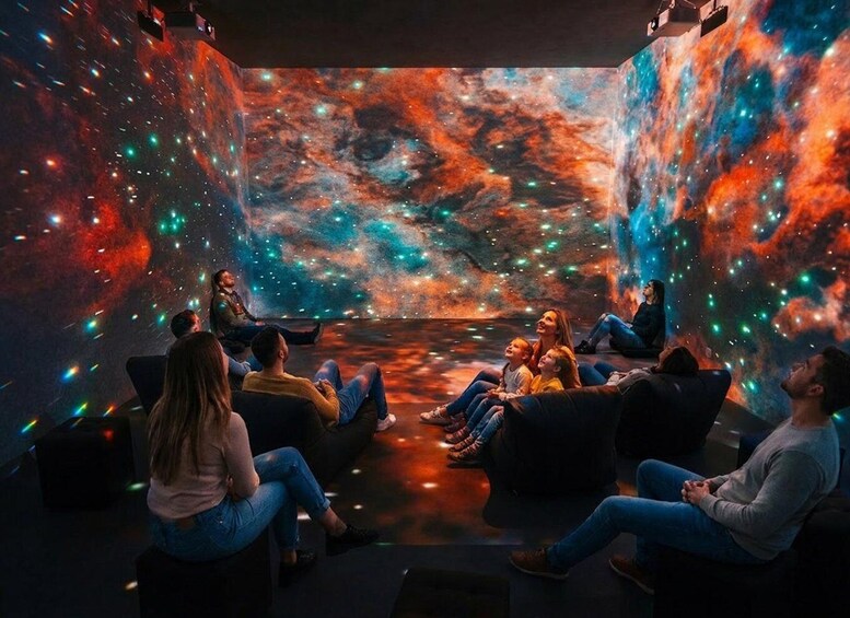 A group of people seated in a room with a cosmic-themed mural. 1