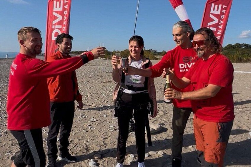 A group of people toasting with drinks on a beach with flags in the background. 2