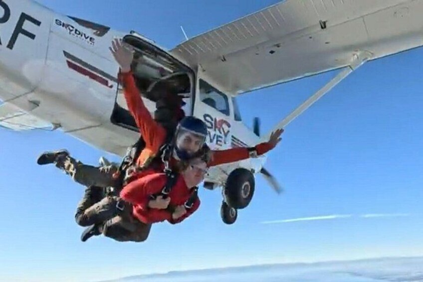 Two skydivers in freefall with a small aircraft in the background. 1