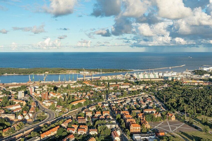 An aerial view of a coastal city with a mix of residential and industrial areas, a large body of water, and a bridge connecting two land masses. 2