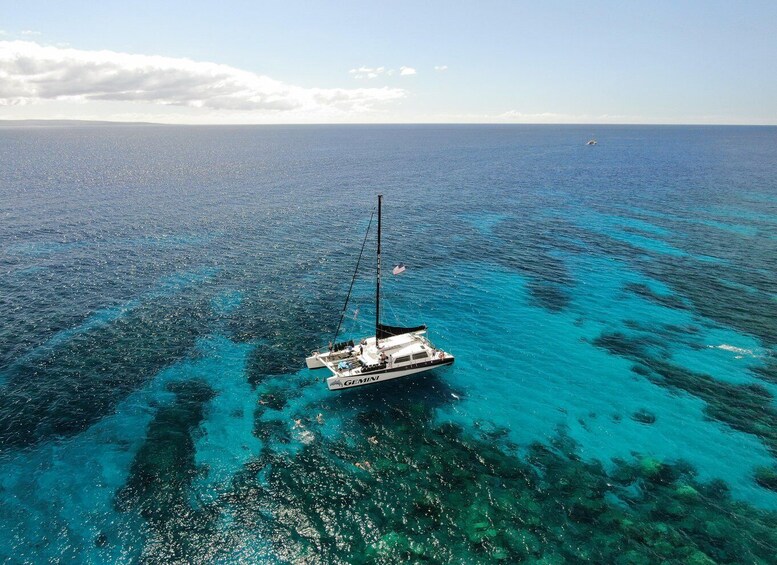 A sailboat named 'GEMINI' anchored in clear blue waters with a distant shoreline. 3