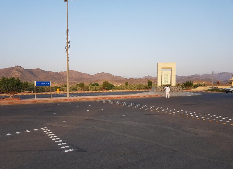 A road with road markings, a blue sign, a monument, and mountains in the background. 4