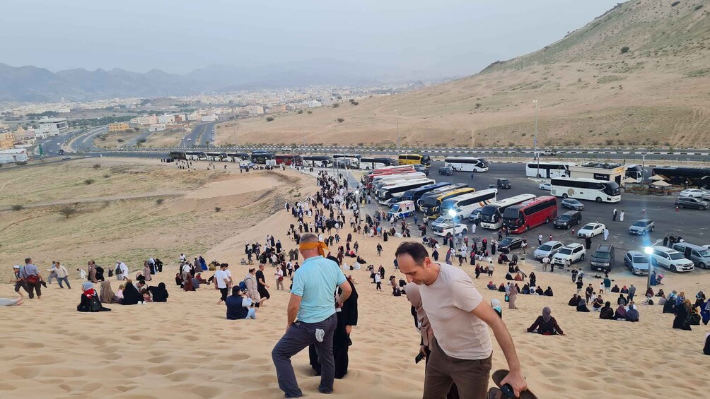 A crowded desert area with people, buses, and vehicles. 2