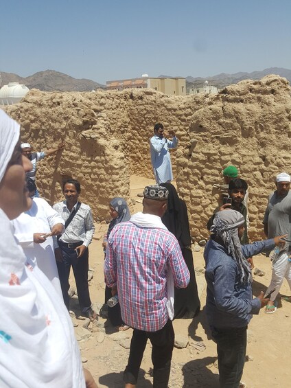 A group of people standing around a large sand structure in a desert landscape with mountains in the background. 3