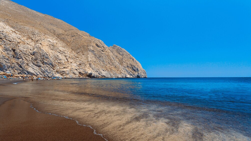 A beach with clear water, a rocky cliff, and a clear blue sky. 2