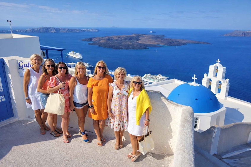 A group of people on a white building with blue domes, overlooking a blue sea and islands. 3