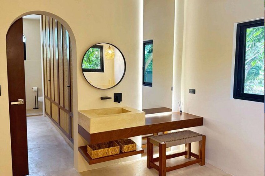 A modern bathroom with a wooden vanity, a round mirror, and a window. 5