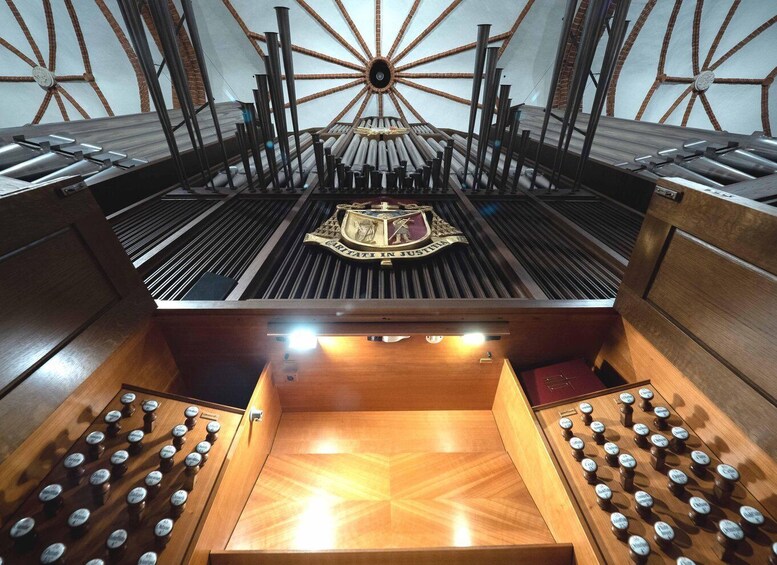 A grand pipe organ with a central emblem, surrounded by wooden panels and multiple pipes. 2