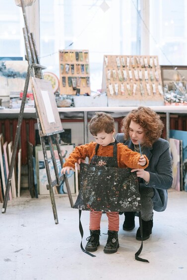 A person holding a child in an art studio with easels and paint supplies. 4