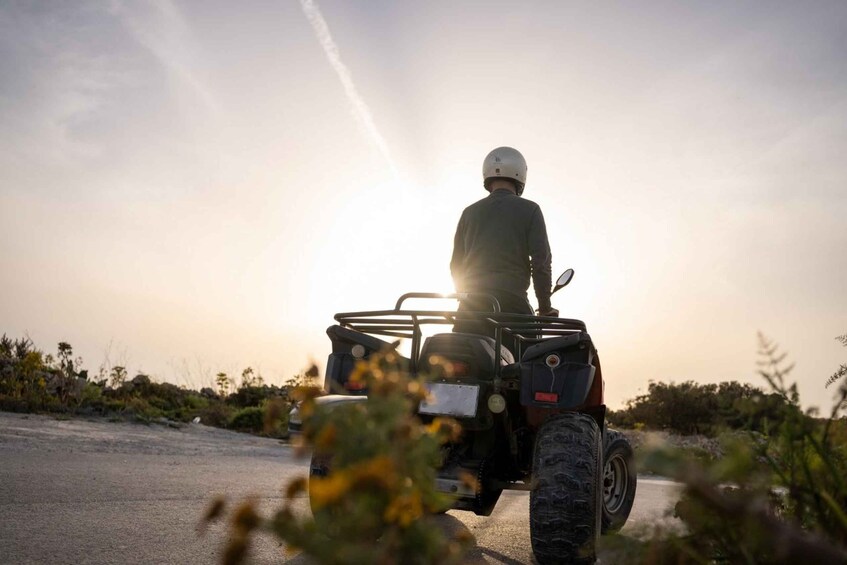 A person riding an ATV on a road with vegetation on the sides. 1