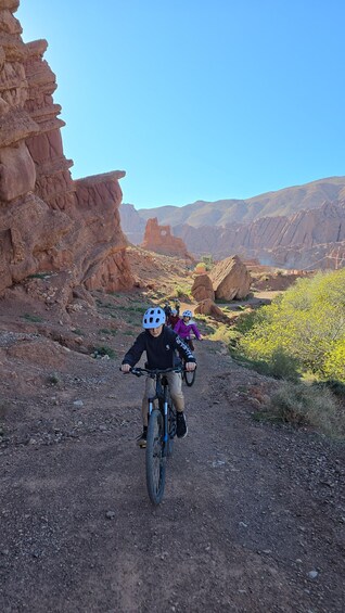 A group of cyclists on a rocky trail surrounded by red rock formations. 1