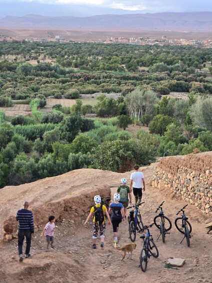 A group of people walking and biking on a dirt path with a mountainous landscape in the background. 3