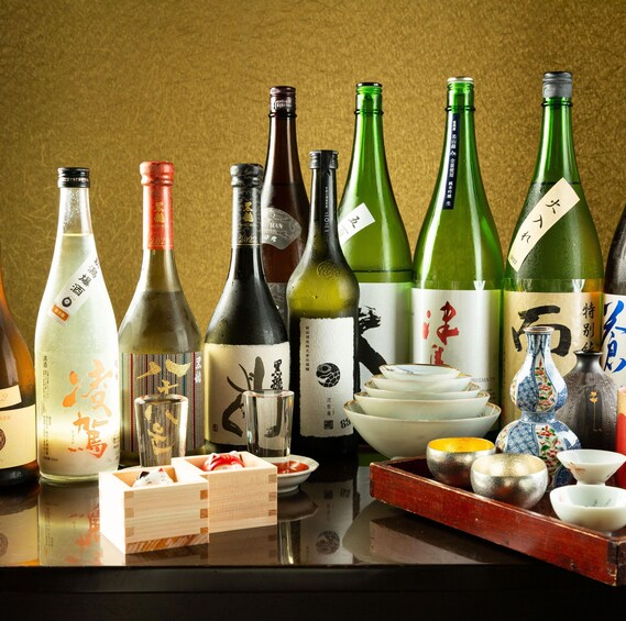 Verschiedene japanische Sake-Flaschen und traditionelle Utensilien für die Teezeremonie auf einem Tisch. 4