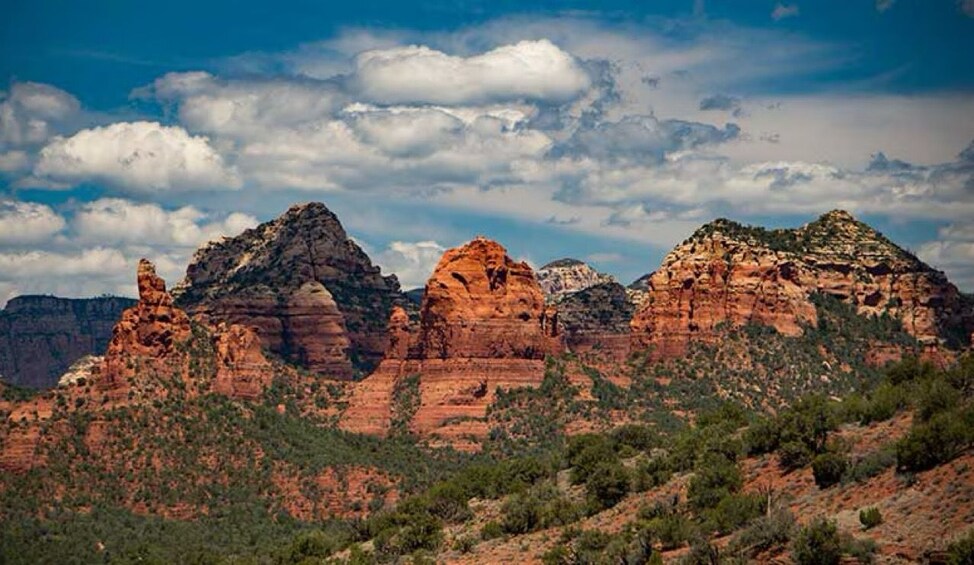 A landscape with red rock formations, green vegetation, and a blue sky with clouds. 3