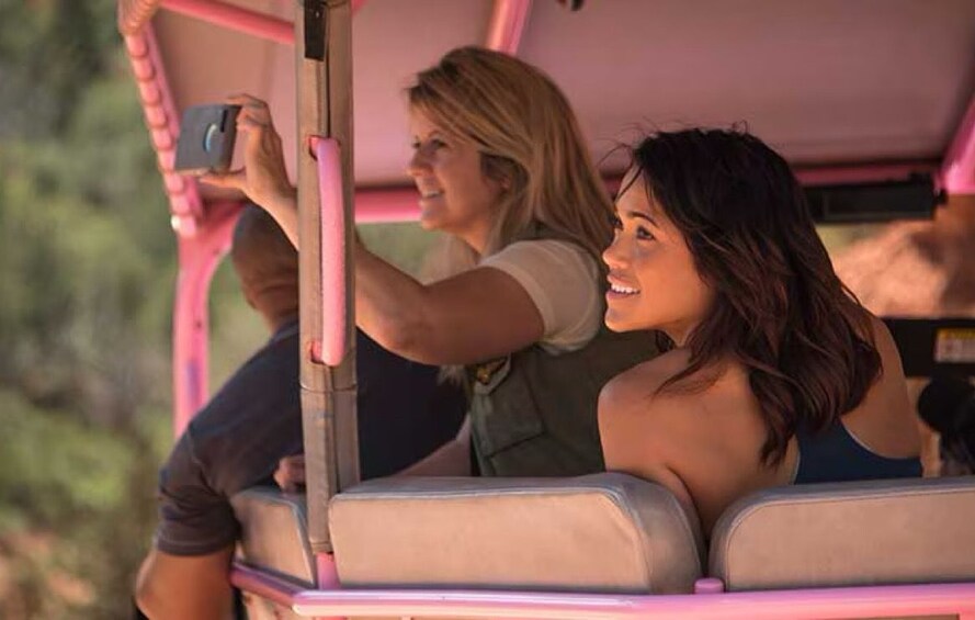 Two people in a vehicle with a pink interior, one holding a camera. 5