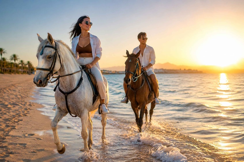 Two people riding horses along a beach at sunset. 1