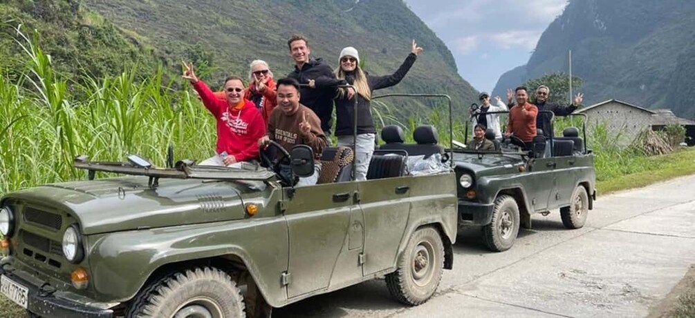 A group of people in a jeep on a rural road with mountains in the background. 1