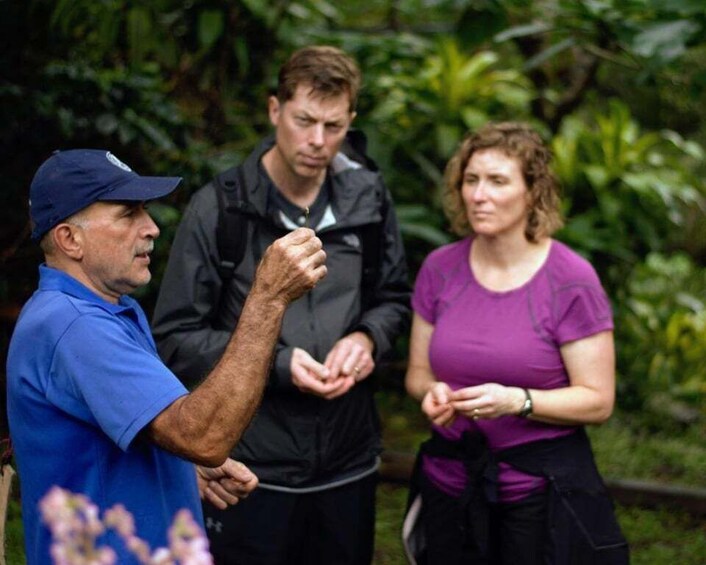 Three people standing outdoors, one in a blue shirt and cap, another in a black jacket, and a woman in a purple shirt. 1