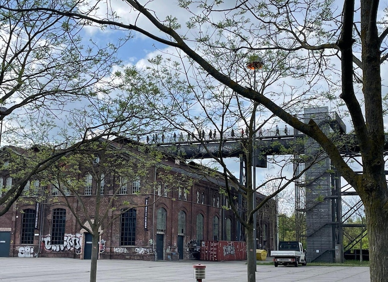 A historic brick building with graffiti, a pedestrian bridge, and a modern building in the background. 1