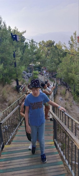 A wooden boardwalk with metal railings, surrounded by trees and a mountainous backdrop. 4