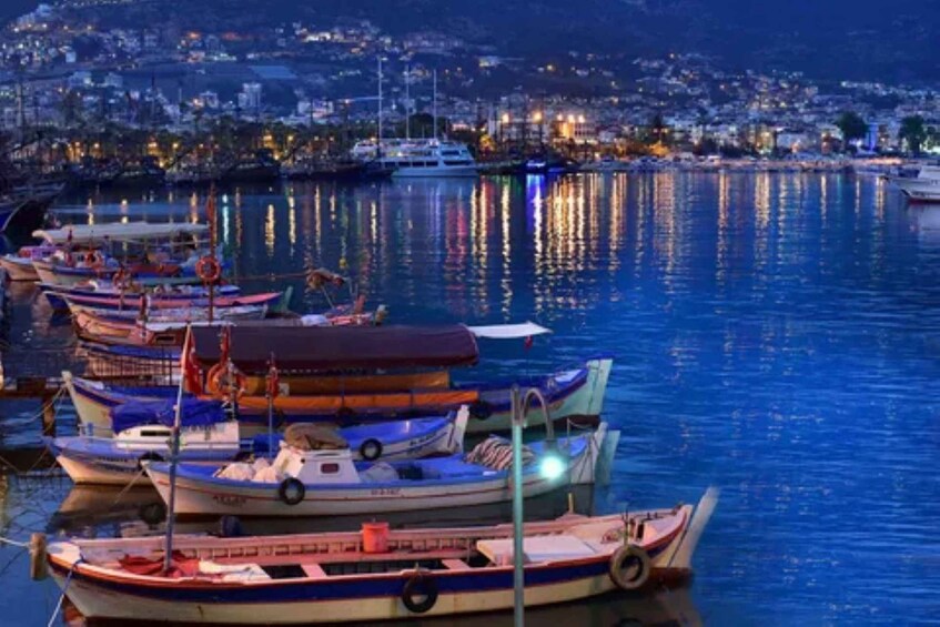 A marina at dusk with boats docked, calm water, and a cityscape in the background. 5