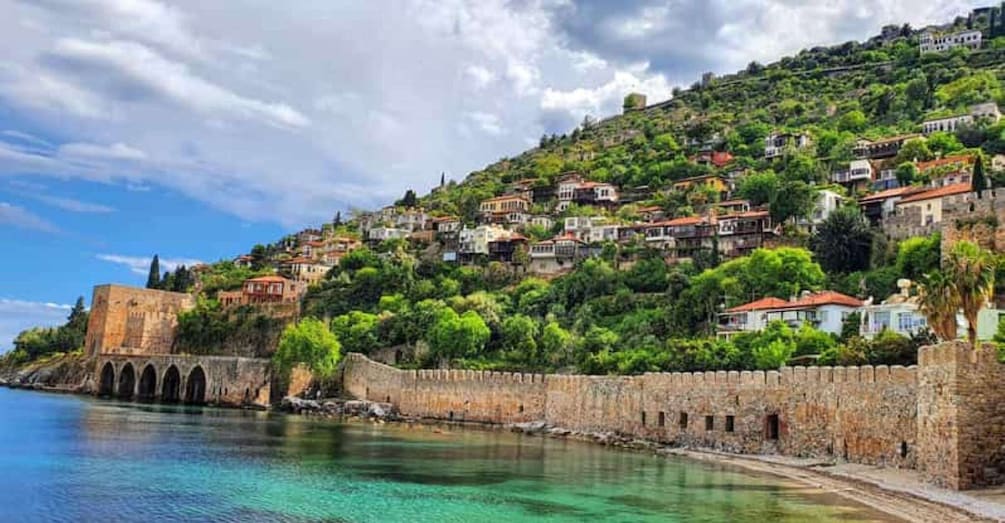 A coastal town with a historic stone wall, clear turquoise waters, and lush green hills. 3