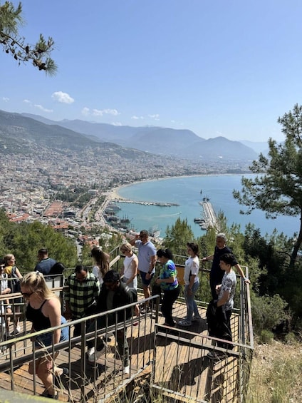 A coastal cityscape with a bay, mountains in the background, and people on a viewing platform. 1