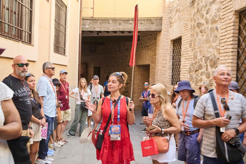 A group of people walking in a narrow street with stone buildings and a red flag. 3