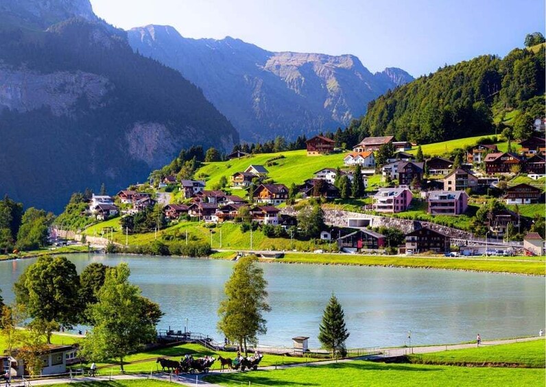 A lakeside village with houses, a bridge, and mountains in the background. 3
