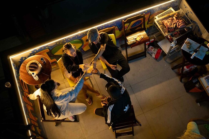 A group of people seated around a table in a brightly lit indoor setting with a food stall in the background. 5