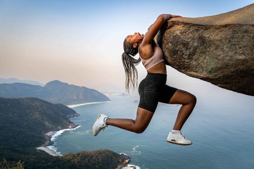 A person climbing a large rock by a coastal cliff. 4