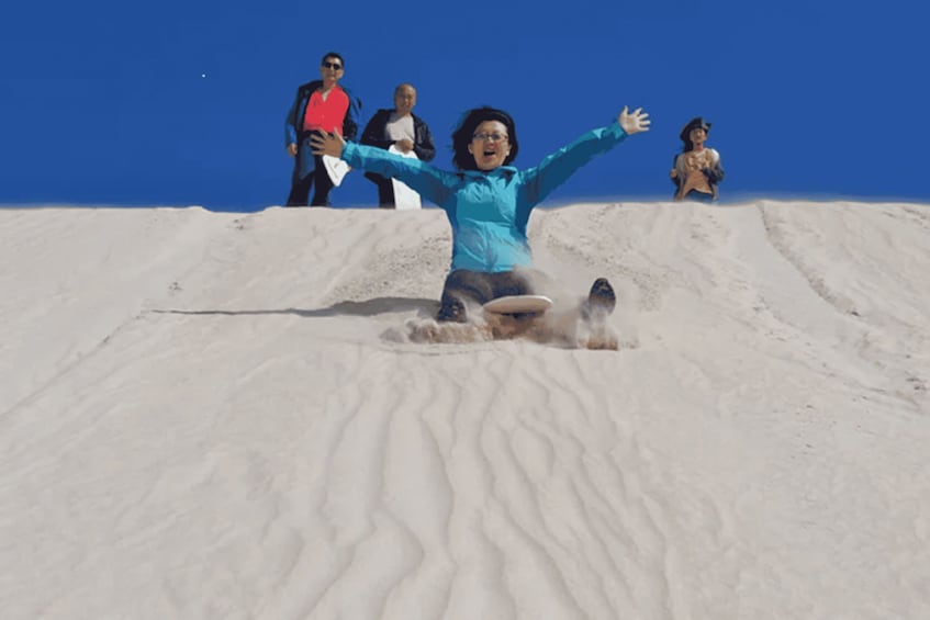 A person sliding down a sandy slope with arms outstretched, surrounded by onlookers. 4