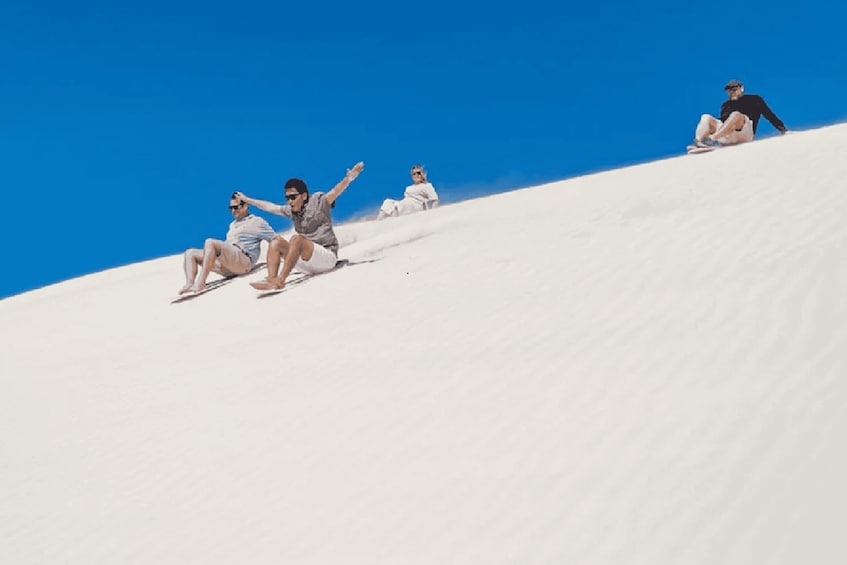 A group of people sitting on a sand dune with a clear blue sky. 5
