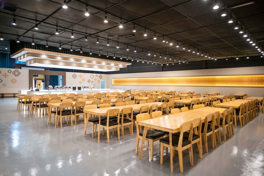 A spacious indoor cafeteria with long wooden tables and chairs, a counter with a menu, and a patterned wall. 5