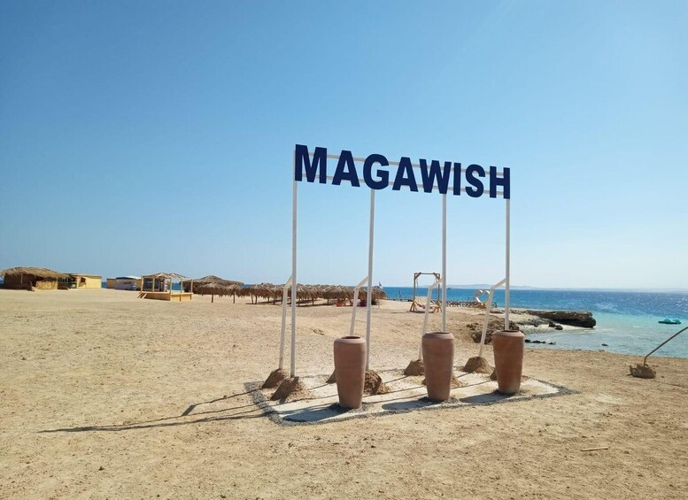 A beach with the sign 'MAGAWISH' and thatched huts in the background. 3