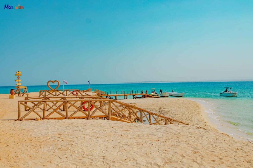 A sandy beach with a wooden pier, boats, and a clear blue sky. 2