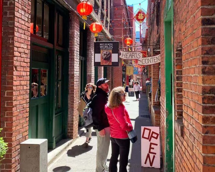 A narrow alley with brick buildings, red lanterns, and signs advertising a restaurant. 1