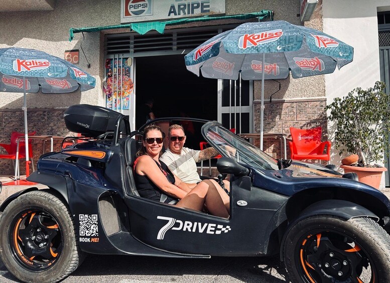 A black 7 DRIVE sports car parked in front of a building with a Pepsi sign. 2