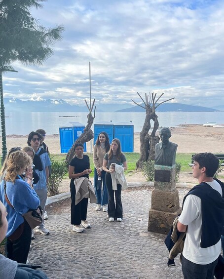A group of people gathered around a statue in a park with a lake and mountains in the background. 5