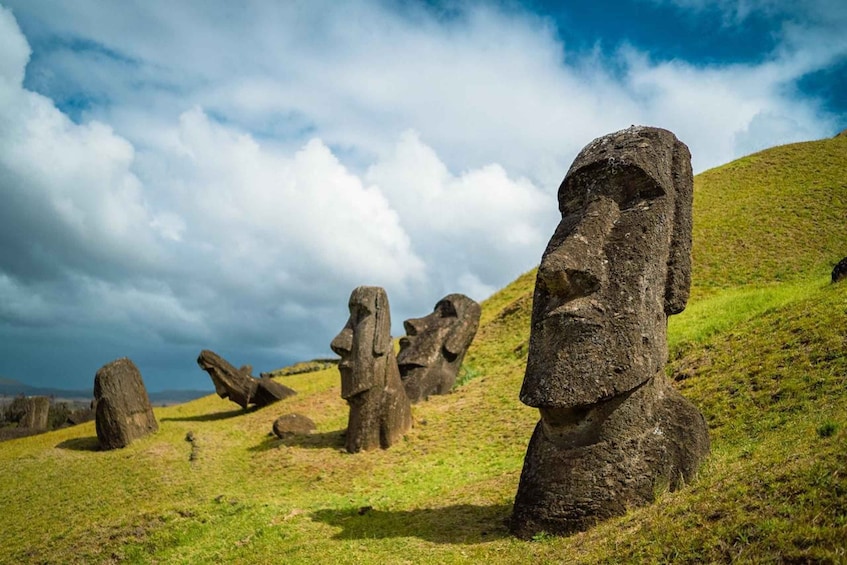 A landscape with large stone statues resembling Moai on a grassy hill under a cloudy sky. 1