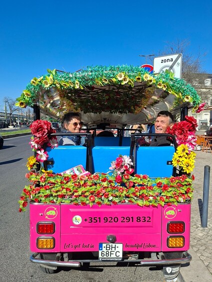 A pink vehicle decorated with flowers and a blue tarp, with a phone number and a license plate visible. 2