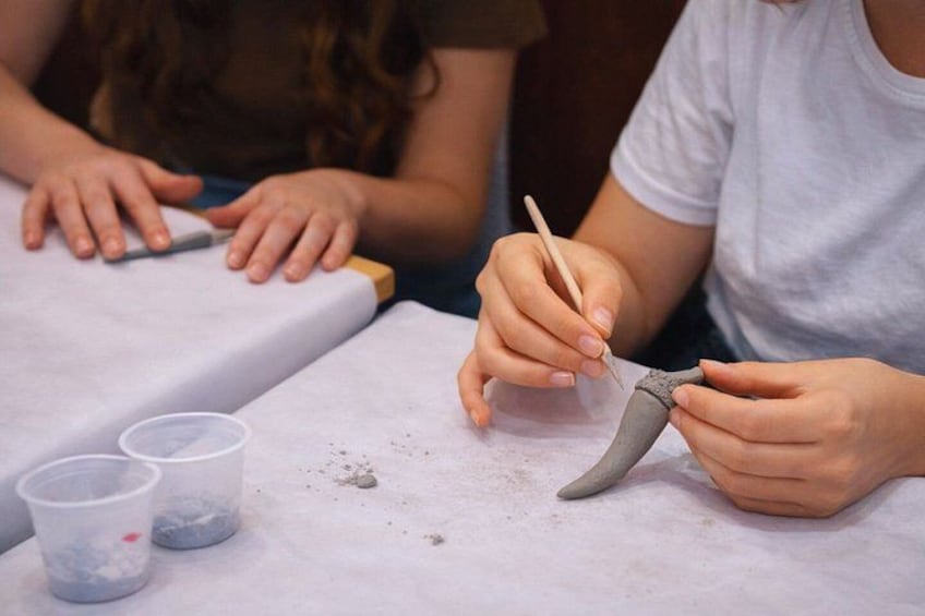 A person sculpting with clay on a table, with two plastic cups and a dustpan nearby. 2