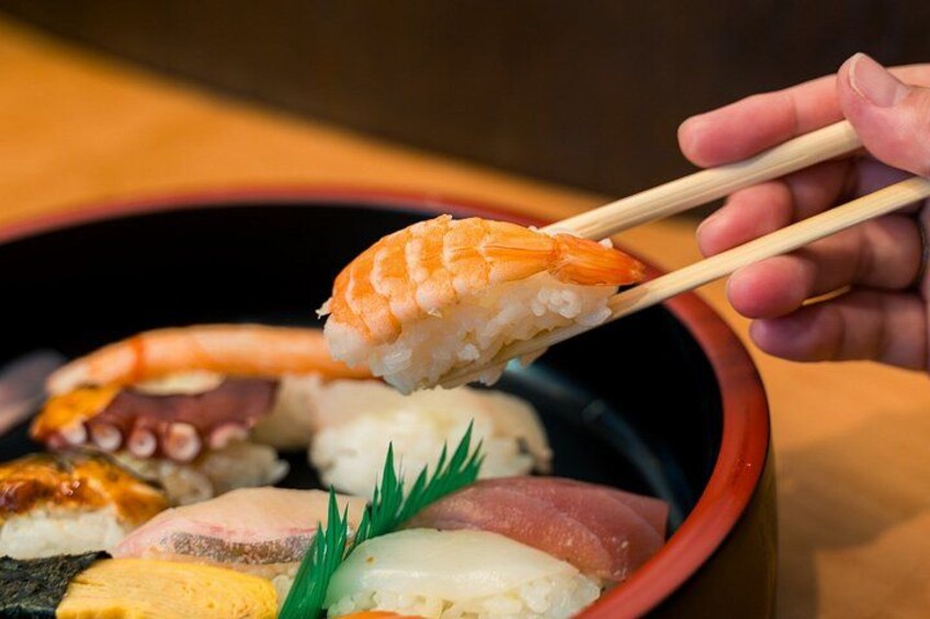 Een schaal sushi met stokjes die een stuk zalmsushi oppakken. 1