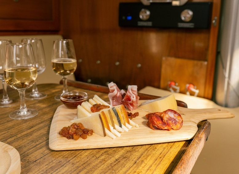 Eine Platte mit Wurstwaren, Käse und Früchten auf einem Holzbrett, dazu Weingläser mit Weißwein. 3
