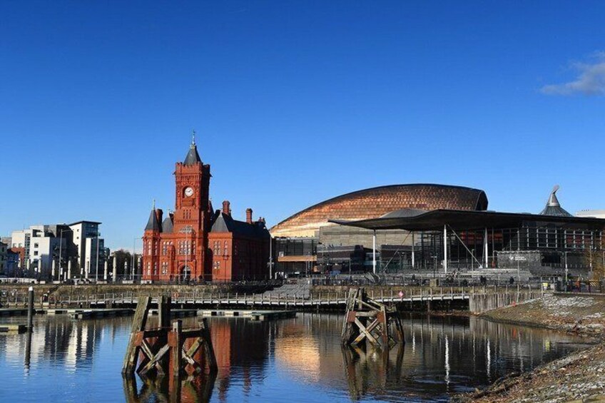 A red brick building with a clock tower and a modern stadium with a curved roof. 2