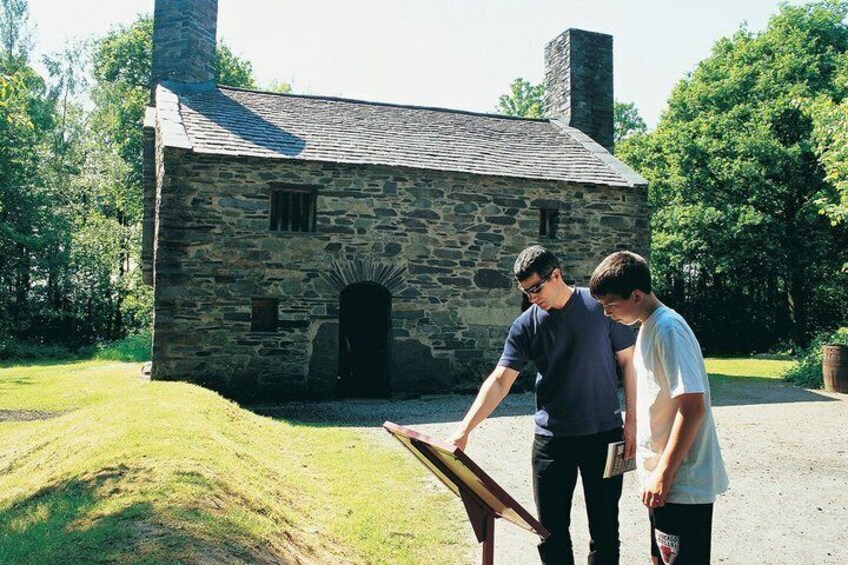 Two people examining a wooden object in front of a stone building with a chimney. 5