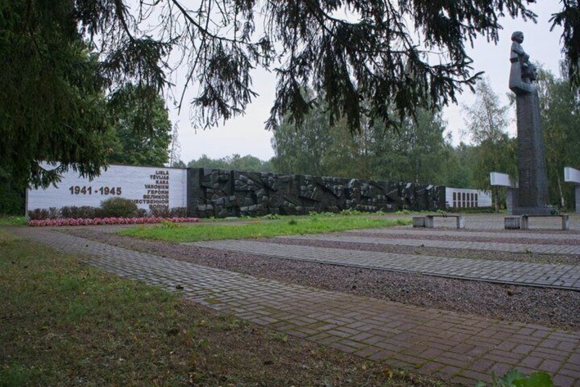 A memorial with a statue, a stone wall, and a paved walkway. 3