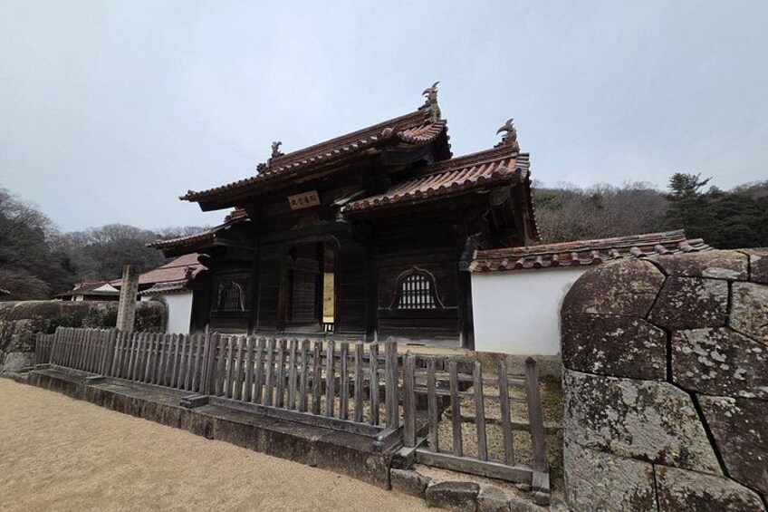 A traditional wooden structure with a tiled roof, surrounded by a stone wall and a wooden fence. 4